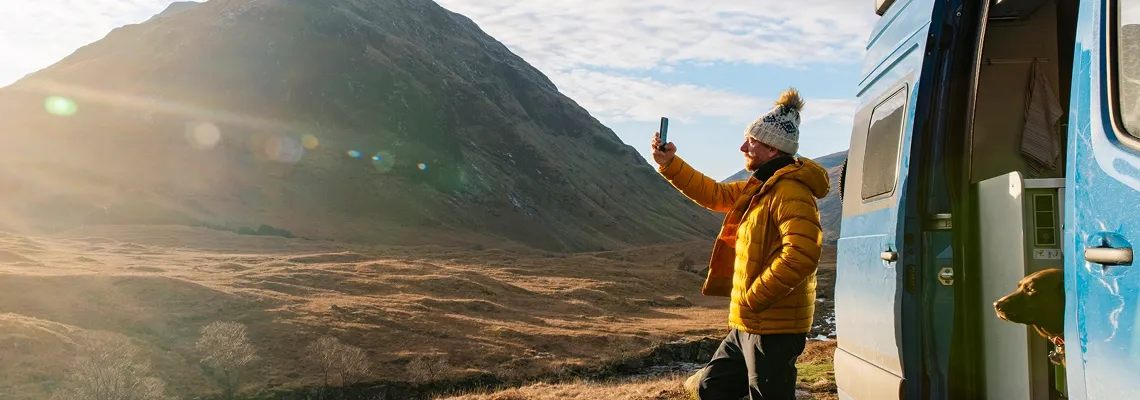 A man and a dog with a van looking toward the sun in a desert landscape