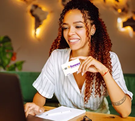 A woman with a laptop holding a Sunward Visa Platinum Rebate Credit Card