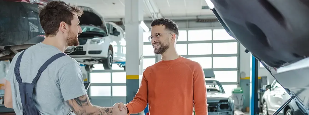 Two men shaking hands. One is a mechanic and they are standing in a car mechanic garage.