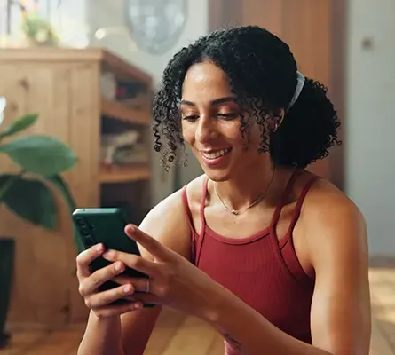 A woman with the sun behind her looking at her phone smiling.