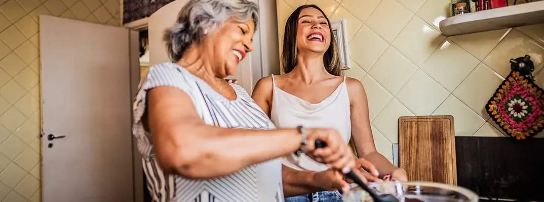 Two women smiling and making food in a kitchen.