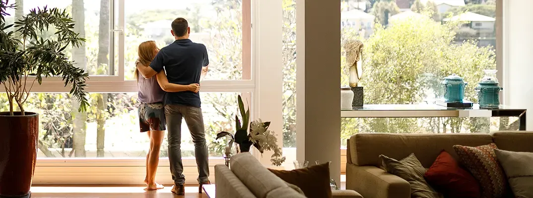 A woman and man standing inside a house by a window.