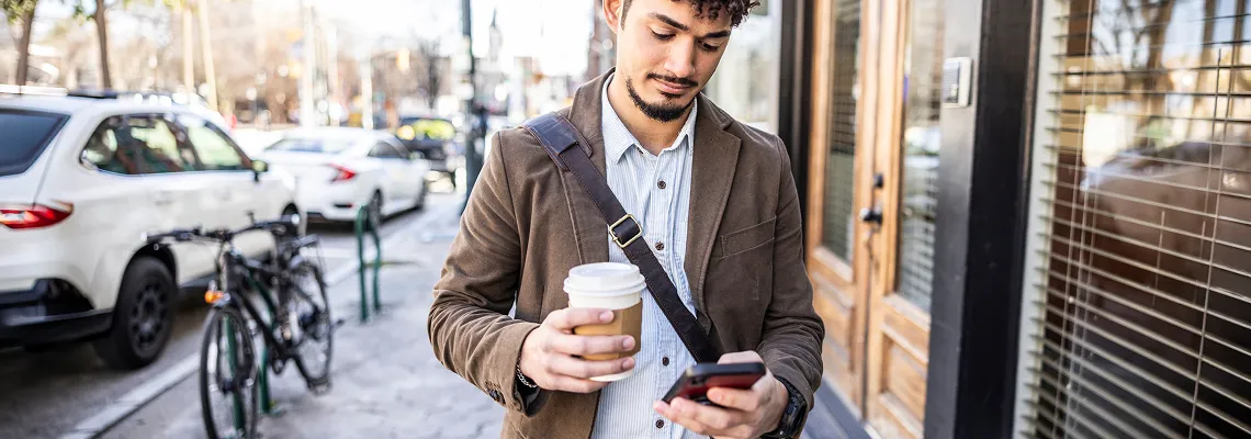 A man walking down the street holding a paper coffee cup and looking at his phone