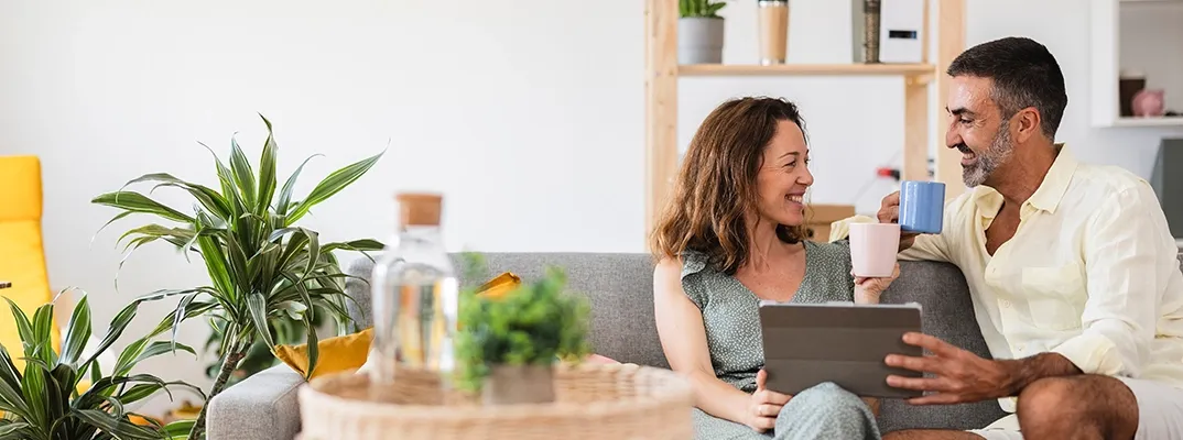 A couple having a cup of coffee looking at each other while holding a tablet