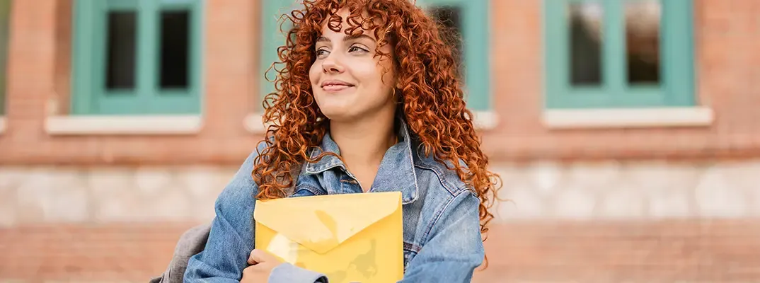 A student holding a folder and smiling as she looks of into the distance
