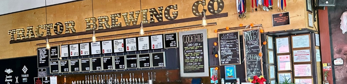 An interior wall with "Tractor Brewing Co." written on it with menu listings and beer taps visible beneath the writing