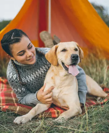 A girl and a dog on a blanket in front of a tent in the wilderness
