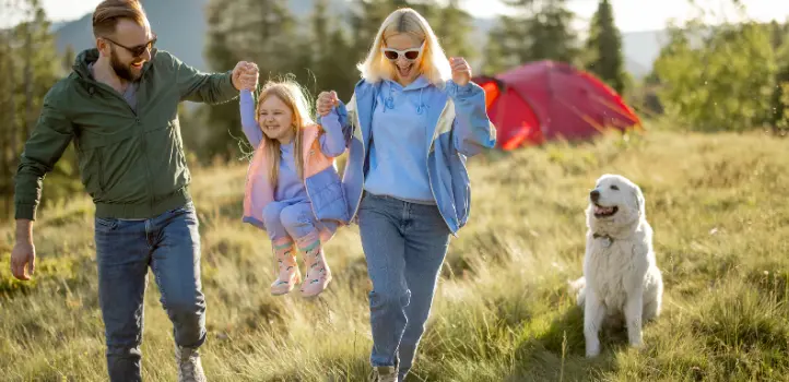 A mother, father, daughter, and their dog in front of a tent in a forest