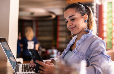 A woman sitting in a lounge area working on her laptop and phone