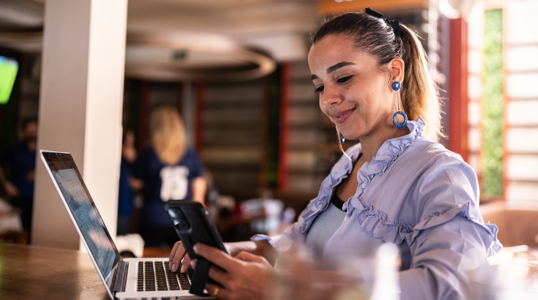 A woman sitting in a lounge area working on her laptop and phone