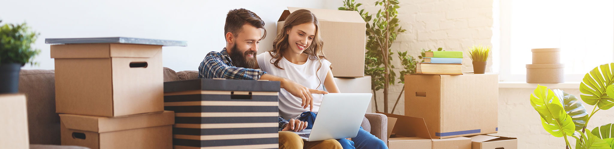 young couple sits among moving boxes looking at a laptop computer