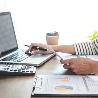 Woman using laptop with calculator, coffee, and financial charts sitting on the table