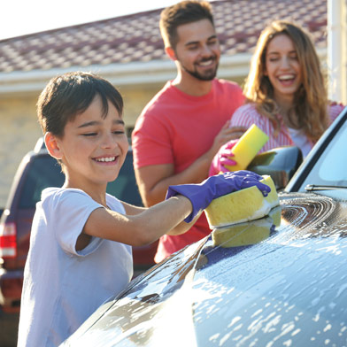 Child washing car outside with parents