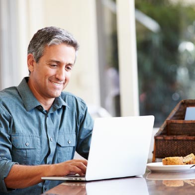 Hispanic man smiling while he uses his laptop at his desk