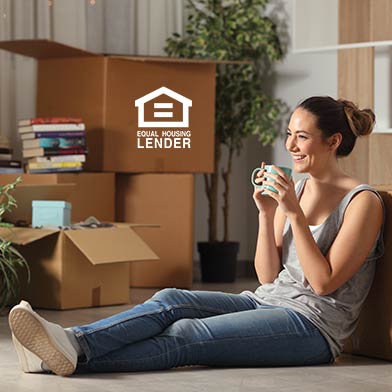 Young woman sitting on floor drinking coffee and surrounded by moving boxes