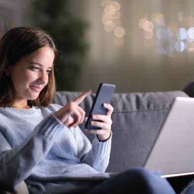 Teen girl scrolling through social media on her cellphone and laptop