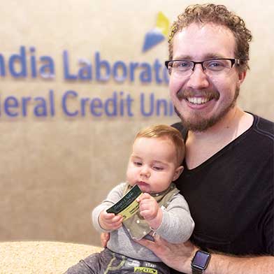 Ryan and Lincoln McCoy posing in front of a Sandial Laboratory Federal Credit Union Logo.