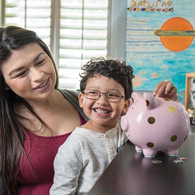 Mom and son adding money to piggy bank.