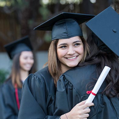 Young woman holding diploma and hugging friend at graduation