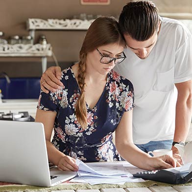 Young woman looking somber while dealing with paperwork at table with significant other hugging her