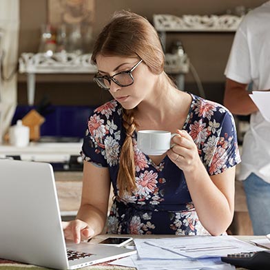 Woman drinking coffee and using laptop to figure out her financial situation