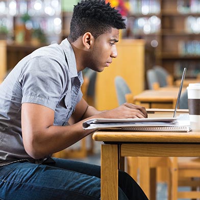 Young college man working on laptop in library