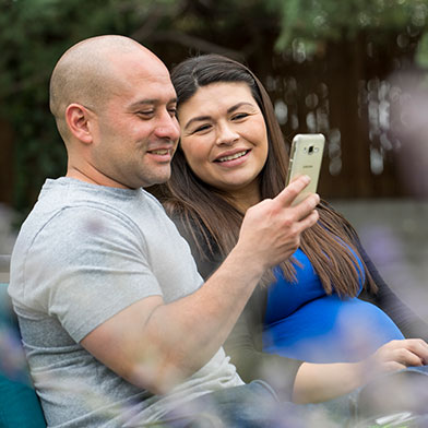 Smiling couple sitting on park bench looking at smartphone.