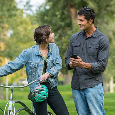 Young woman with bike and man holding cellphone talking outside