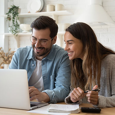 Young couple smiling while looking at computer and paying bills