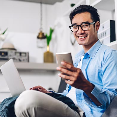 Young man with laptop smiling and using cell phone