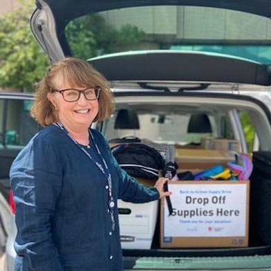 Sunward Business Manager, Julia, smiling and posing next to boxes full of donations