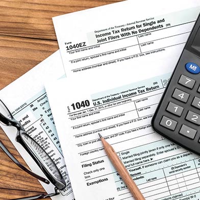 Tax paperwork with a calculator, glasses, and pencil laying on top