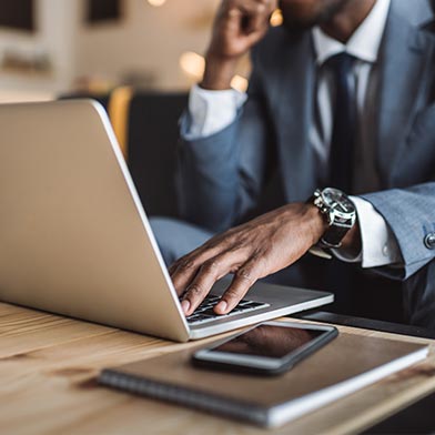 Close up of man with watch using laptop with his phone beside him