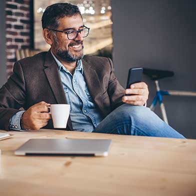 Smiling man holding a cup of coffee and looking at his smartphone.