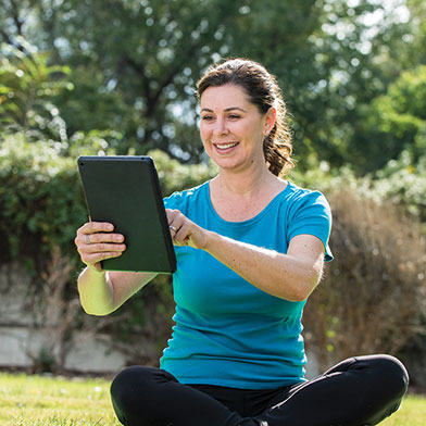 Woman sitting on grass using tablet outside