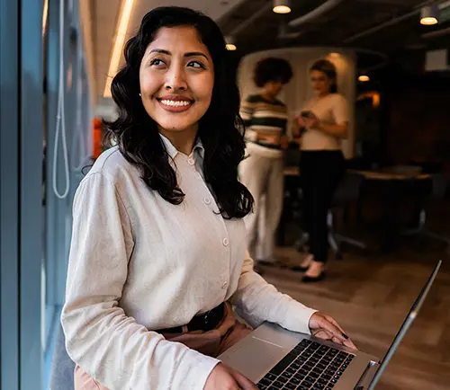 A well-dressed, smiling woman sitting with a laptop in an office setting
