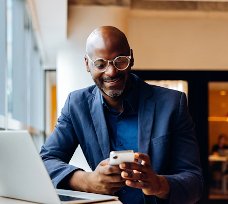 A well-dressed man sitting in front of a laptop while looking at his phone