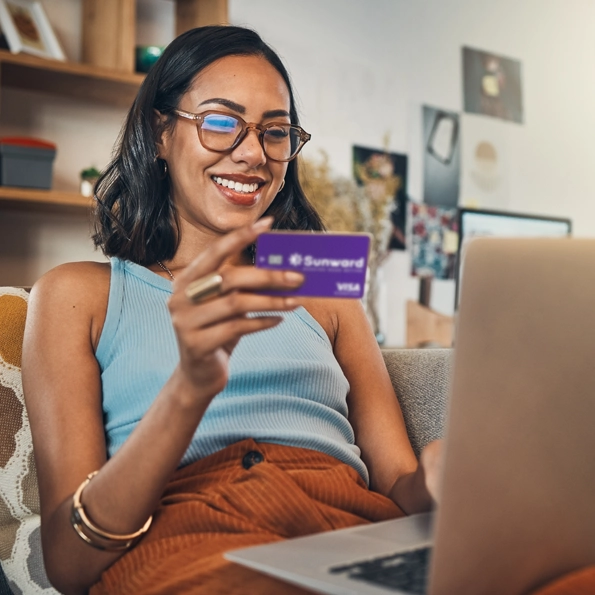 A woman with a laptop holding a Sunward Visa Signature Credit Card
